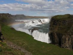 A parkolás után hirtelen előtűnő impozáns Gulfoss vízesés elkápráztat. Hosszú percekig nézem, még magamba sem tudok beszélni a meglepetéstől. A tömbház magasságú vízeséssel kapcsolatos érdekes történet olvasható a helyszínen: innen indult Izland első környezetvédelmi mozgalma. Az 1920-as években vízerőművet próbáltak létrehozni, de Sigríður Tómasdóttir, az egyik befektető lánya ellenszegült. Szerencsére a vízesést és környékét 1979-ben természetvédelmi területté nyilvánították, így a tervezett befektetés meghiúsult. Az országban továbbra is nagy a nyomás a természet adta energiaforrások kihasználására, de amint azt több helyen láthattuk kiplakátolva, jelenleg Izland szükségleteinek 100 százalékát (!) környezetkímélő forrásokból meríti: geotermális, szél, hő- és vízenergia felhasználásával. A napsütés csodálatos szivárvánnyal öleli át ezt a természeti csodát. Még a legkevésbé romantikus férfi is elérzékenyül a látványon..
